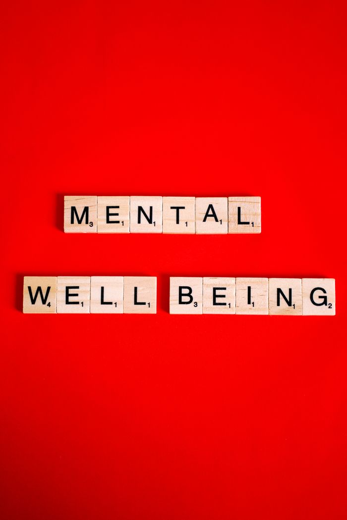 services-04 Scrabble tiles spelling 'mental well-being' on a red background, symbolizing mental health.